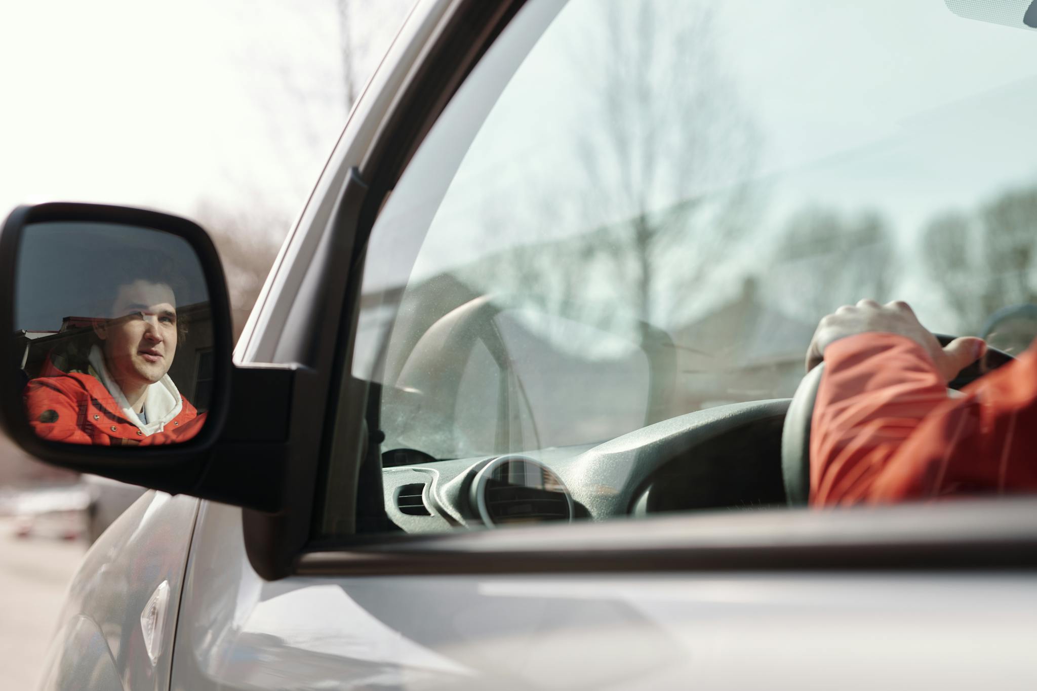 Close-up of a man reflected in a car side mirror while driving on a sunny day.