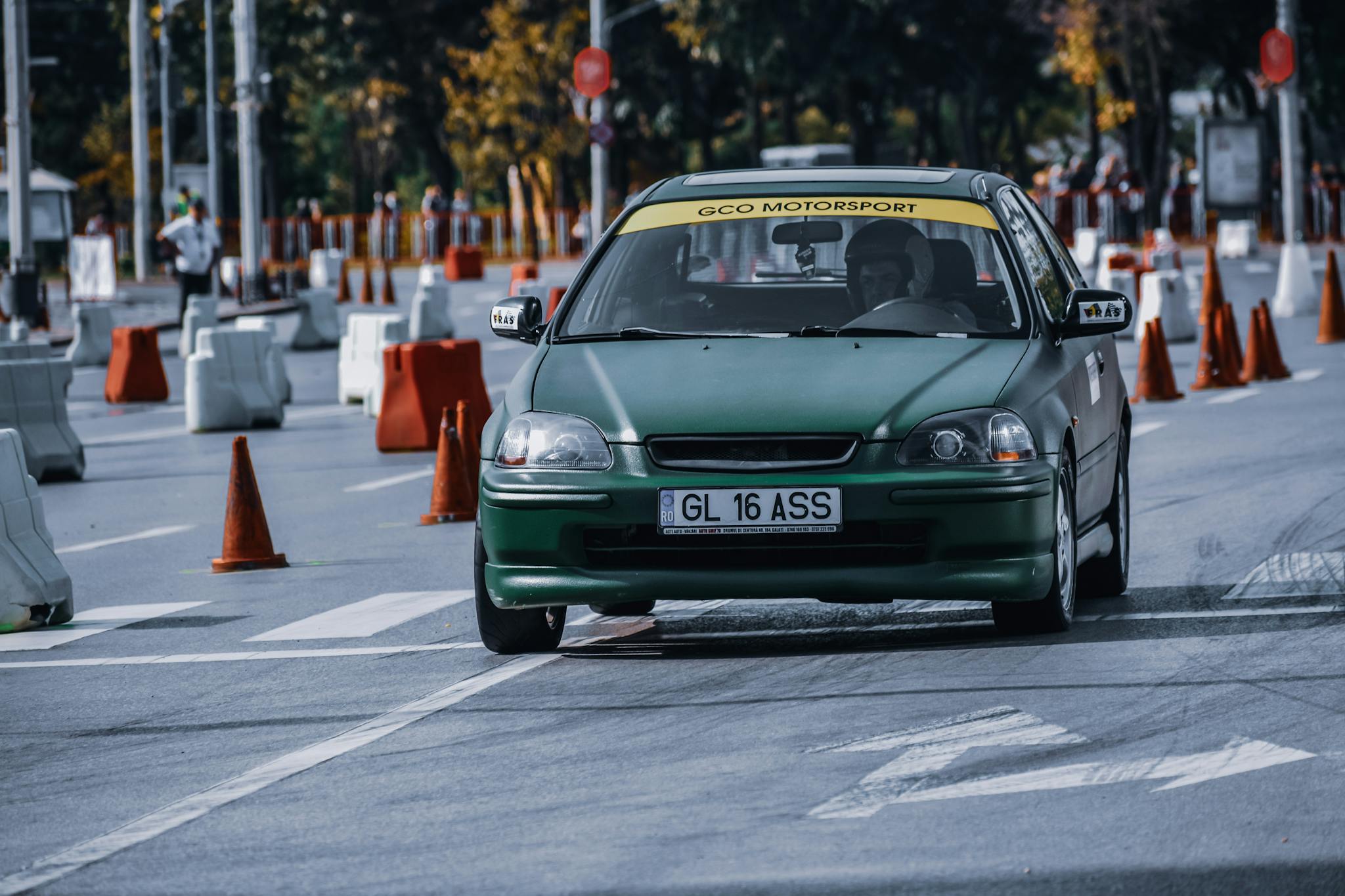 Dynamic shot of a green car on a racetrack amidst traffic cones in an urban setting.
